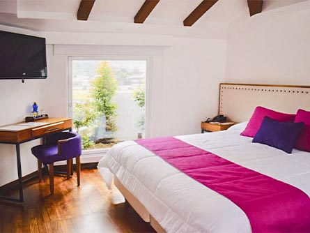 A cozy room with wood flooring and a pink and purple motif at the Sangay Hotel in Baños.