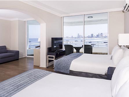 A spacious room with two beds and a view of the ocean and skyline at the Terrado Suites in Iquique.