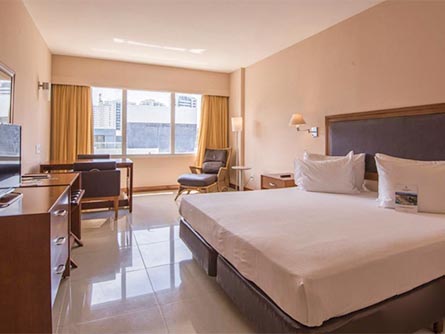 A spacious room with a large bed, an entertainment center and table at Vila Gale hotel in Salvador.