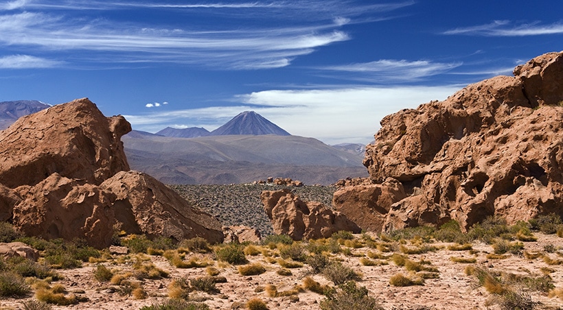 Rock formations and desert landscape with a volcano visible in the distance in the Atacama Desert.