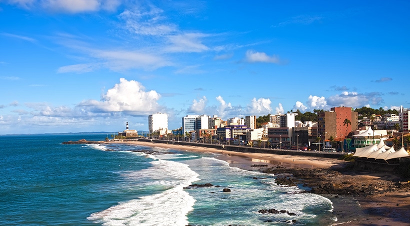 A beach next to the city of Salvador de Bahia, with the Barra lighthouse visible in the distance.