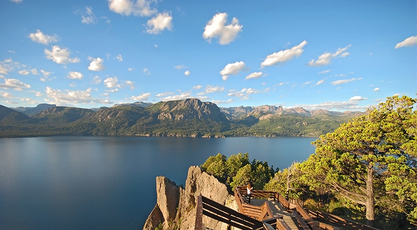 A visitor on a pathway overlooking a scenic lake surrounded by mountains near Bariloche.