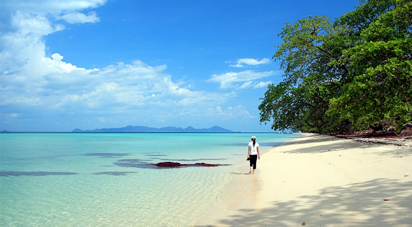 A visitor walks along a picturesque beach with stunning blue water and tropical trees in Búzios.