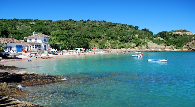 Visitors on a beach in Buzios with crystal blue water and surrounded by lush vegetation.