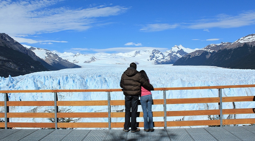 A couple on a walkway looking out at the enormous Perito Moreno glacier in Argentine Patagonia.
