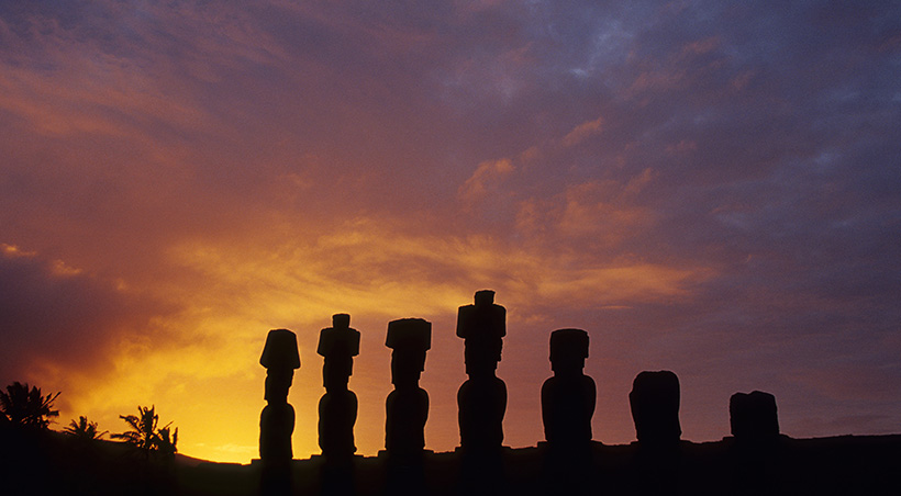 The sun setting over a series of moais, the mysterious stone figures found throughout Easter Island.