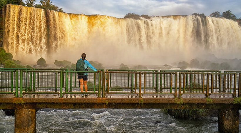 A visitor standing on a small bridge and admiring the awe-inspiring beauty of Iguazu Falls.