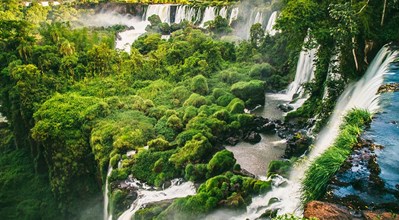 Lush vegetation and a stepped waterfall with more waterfalls in the background at Iguazu Falls.