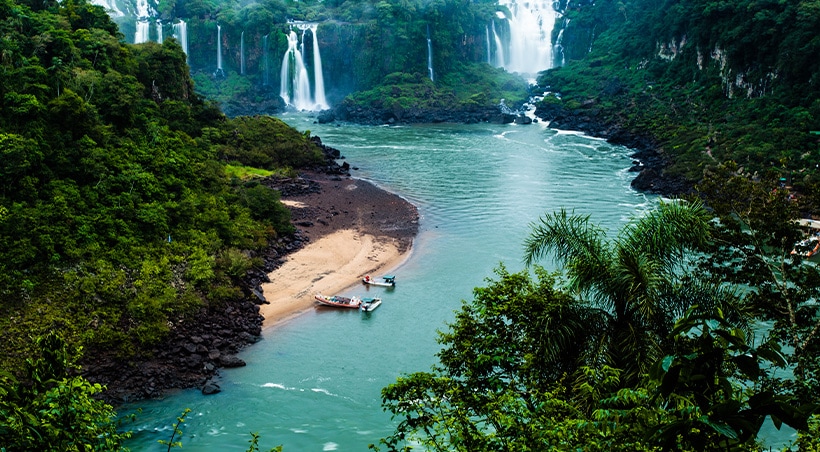 Small boats docked at a beach surrounded by the lush jungle vegetation of Iguazu Falls.