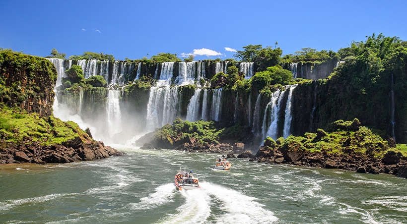 A couple of small boats navigating the water at the foot of the famous Iguazu Falls.