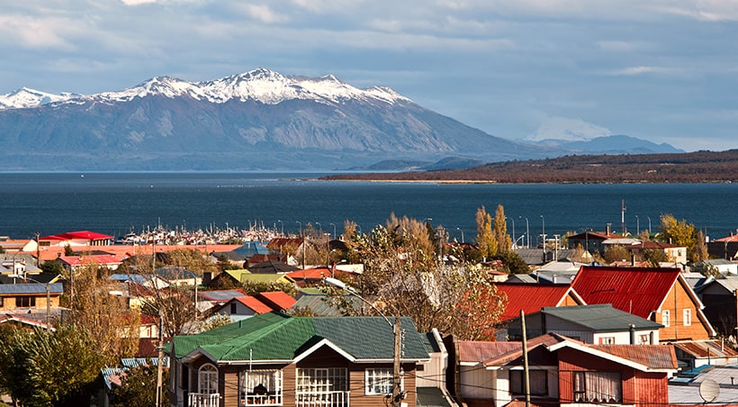 Rooftops of colorful traditional houses with snow-capped mountains overhead in Puerto Natales.