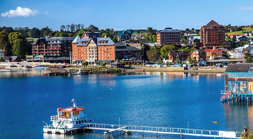 Houses and buildings lining the port of Puerto Varas and a small boat docked in the water.