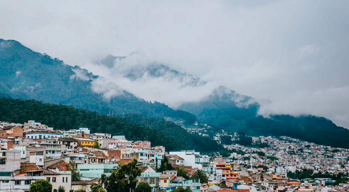 Mountainsides shrouded in clouds and covered in green forest, overlooking the city of Quito.