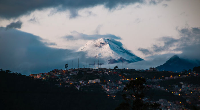Lights dotting the Quito cityscape with the massive snow-capped Cotopaxi volcano towering overhead.