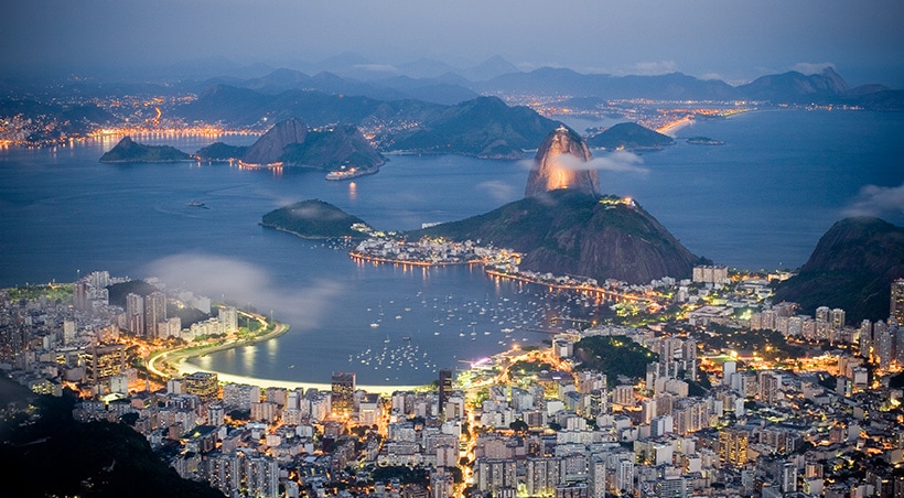 Rio de Janeiro lit up at night, with the iconic Sugarloaf Mountain towering over the city.