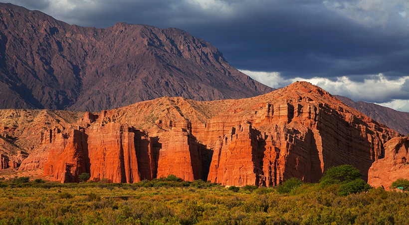 Stunning red rock formations overlooked by a mountain with an ominous dark sky above.