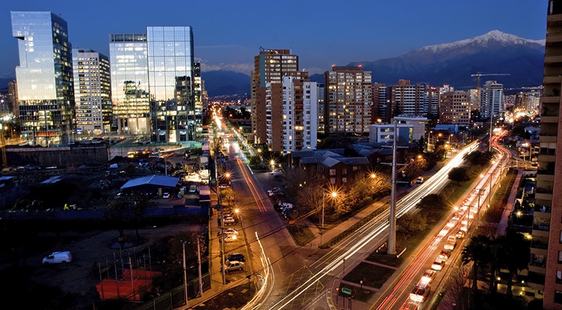 An intersection in Santiago with modern buildings and a snow-capped Andean peak visible.