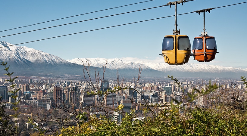 A pair of cable cars overlooking the city of Santiago with the Andes Mountains as a backdrop.