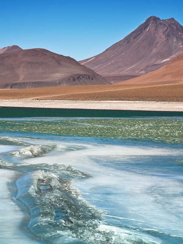The shimmering water of a lagoon overlooked by red and orange mountains in Chile's Atacama Desert.