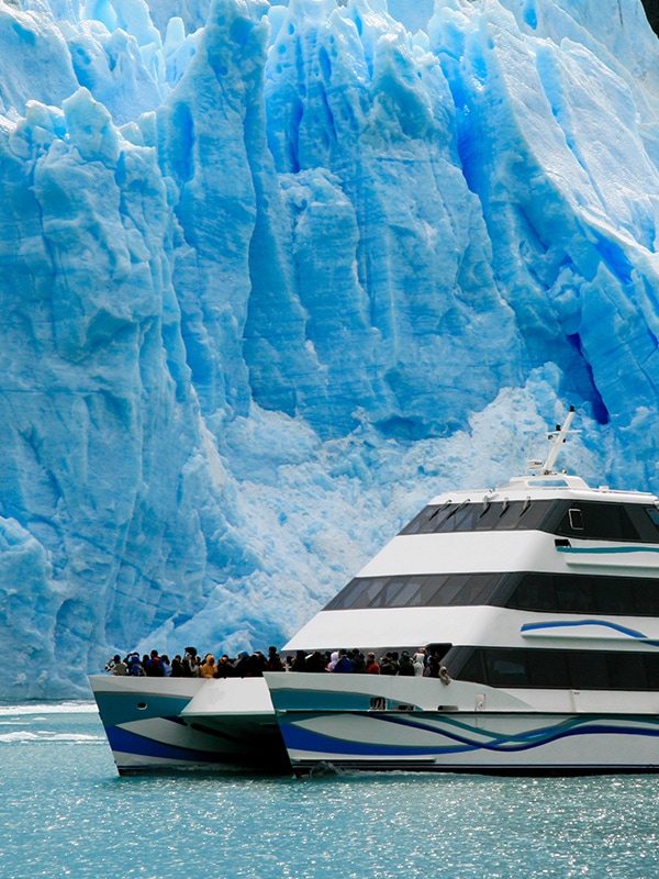 A cruise boat full of tourists admiring a massive blue glacier in Los Glaciares National Park.