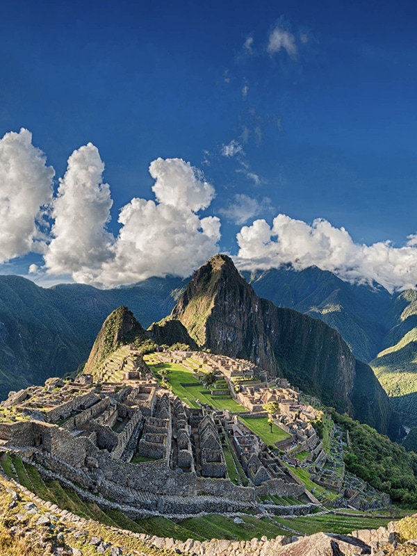 The Inca ruins of Machu Picchu with the Andes Mountains as a backdrop on a partly cloudy day.