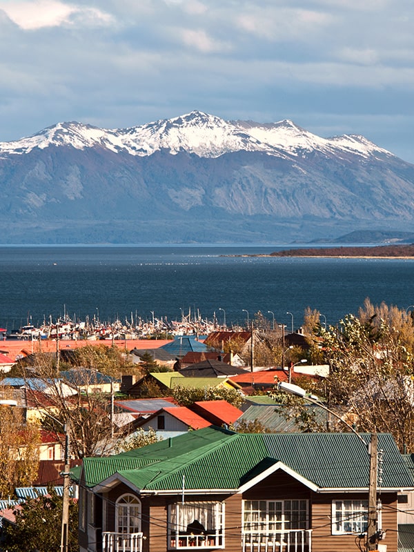 Rooftops of colorful traditional houses with snow-capped mountains overhead in Puerto Natales.