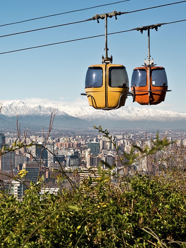 A pair of cable cars overlooking the city of Santiago with the Andes Mountains as a backdrop.
