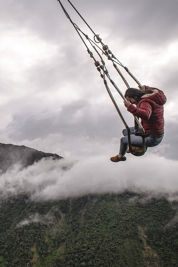 A woman swinging above the cloud forest on the Swing at the End of the World in Baños.