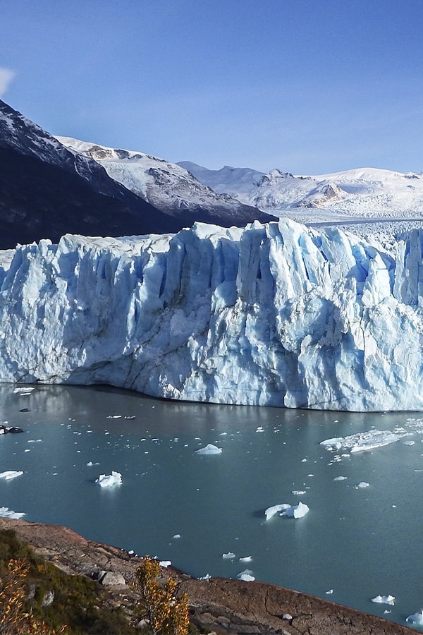 The massive blue-tinted Perito Moreno glacier surrounded by snow-covered hills and mountains.