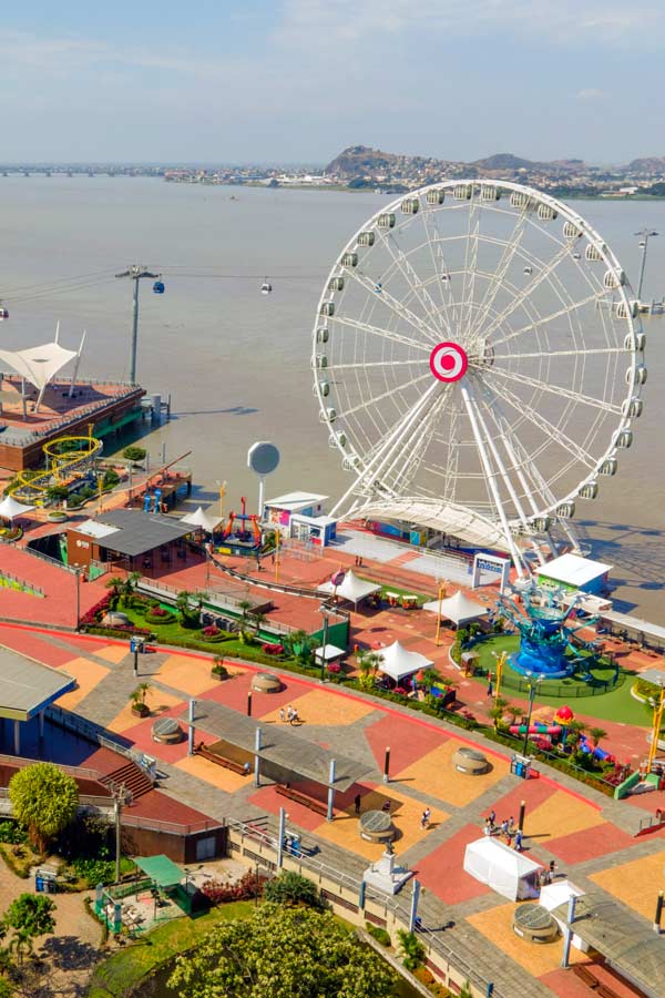 A panoramic view of Guayaquil with a ferris wheel and a cable car line stretching across the water.