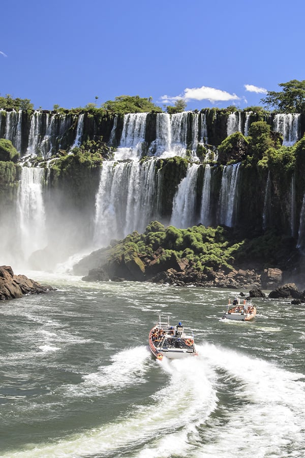 A pair of boats navigating the waters below several waterfalls at the famous Iguazu Falls.