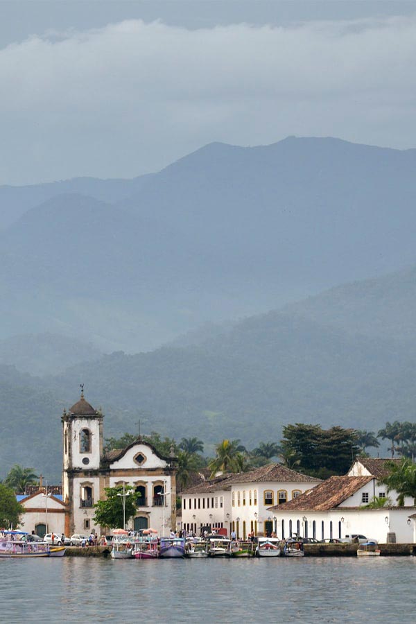 Boats in the water near the St. Rita church in Paraty, with forest-covered hills surrounding.