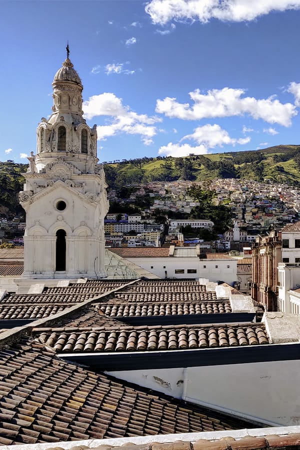 The Metropolitan Cathedral of Quito surrounded by green hillsides lined with houses.