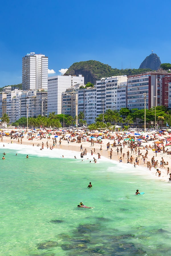 A beach in Rio with a row of modern buildings behind it and Christ the Redeemer in the distance.