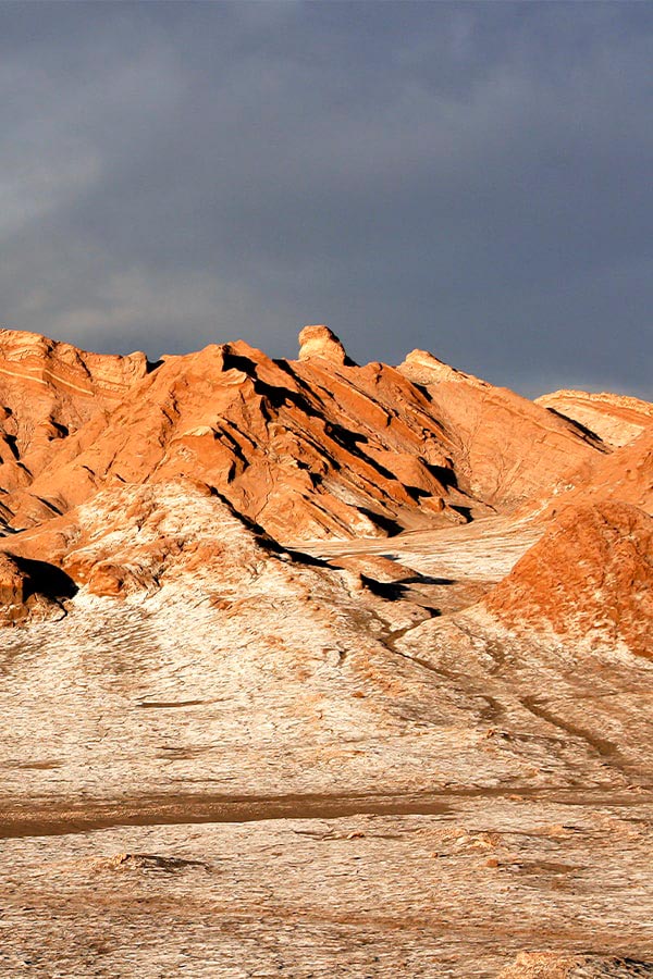 Jagged red rock formations covered in frost underneath a dark sky in the Atacama Desert.