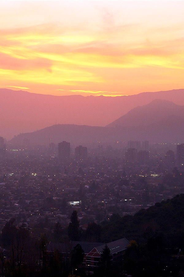 The sun setting over the Santiago skyline, with the Andes Mountains visible in the background.
