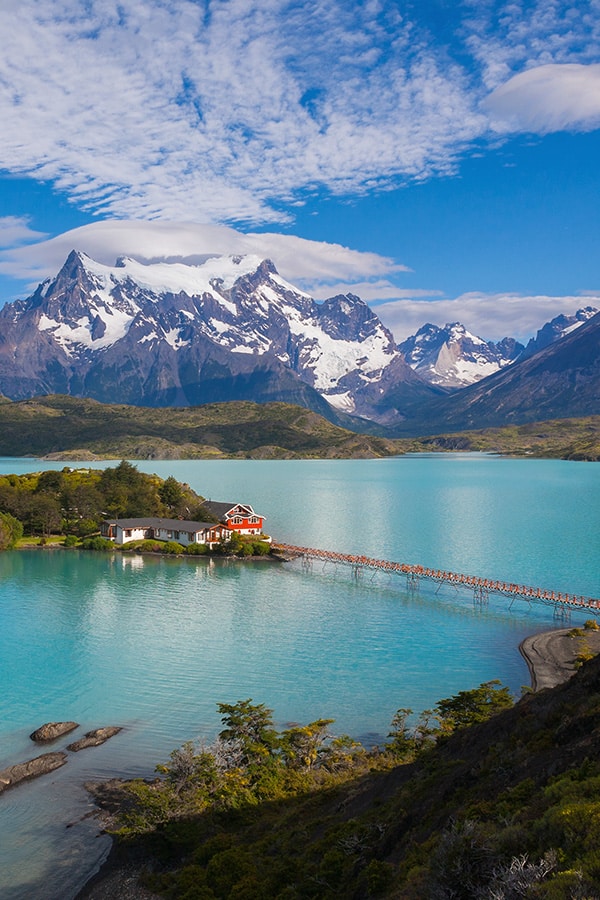 Scenic houses on a blue-tinted lake with snow-capped mountains at Torres del Paine National Park.