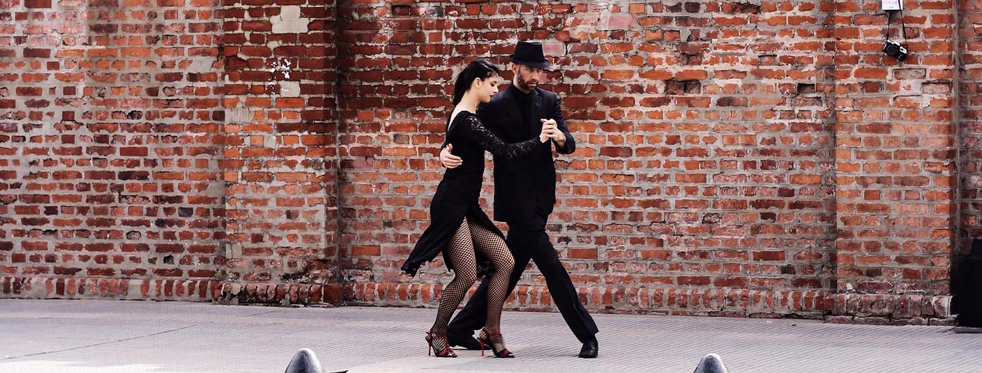 A pair of dancers performing the tango in front of a brick wall in Buenos Aires.