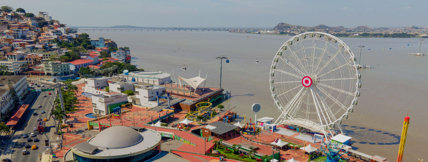 A panoramic view of Guayaquil with a ferris wheel and a cable car line stretching across the water.