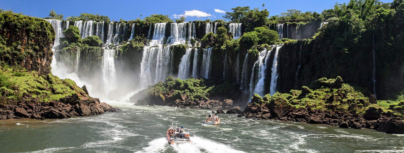 A pair of boats navigating the waters below several waterfalls at the famous Iguazu Falls.