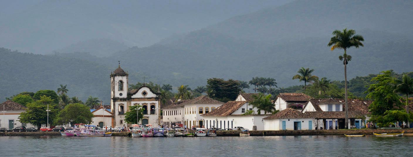Boats in the water near the St. Rita church in Paraty, with forest-covered hills surrounding.