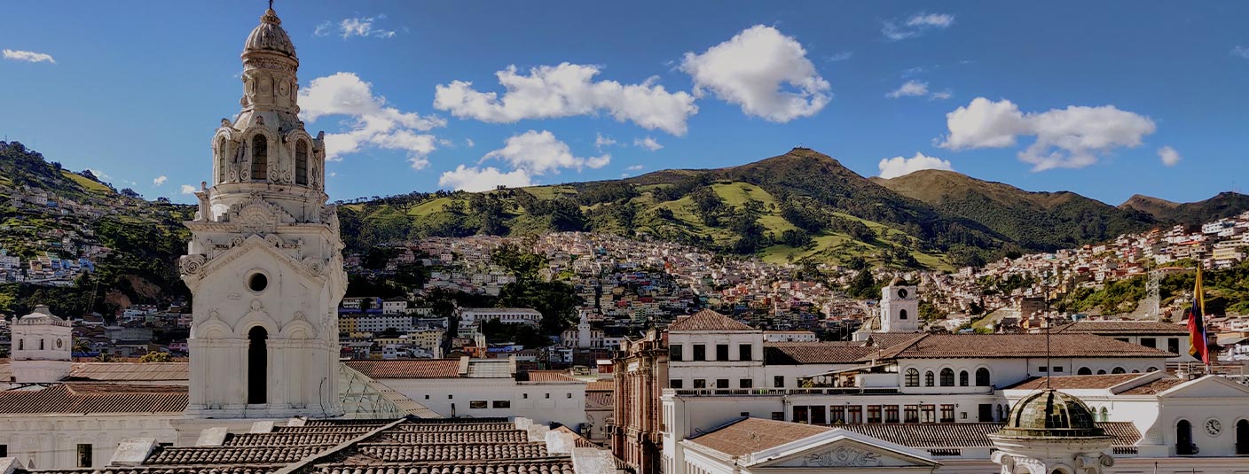 The Metropolitan Cathedral of Quito surrounded by green hillsides lined with houses.