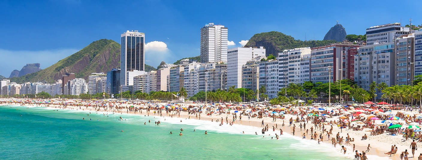 A beach in Rio with a row of modern buildings behind it and Christ the Redeemer in the distance.