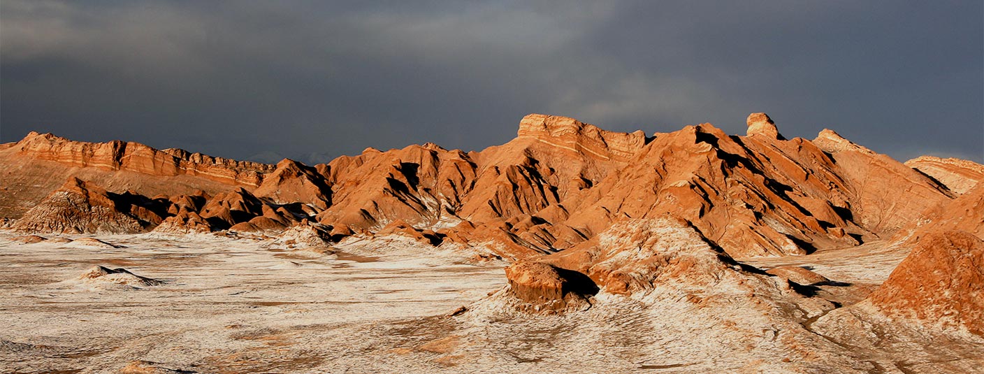 Jagged red rock formations covered in frost underneath a dark sky in the Atacama Desert.