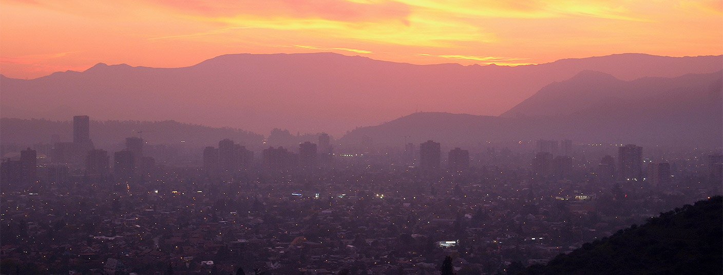 The sun setting over the Santiago skyline, with the Andes Mountains visible in the background.