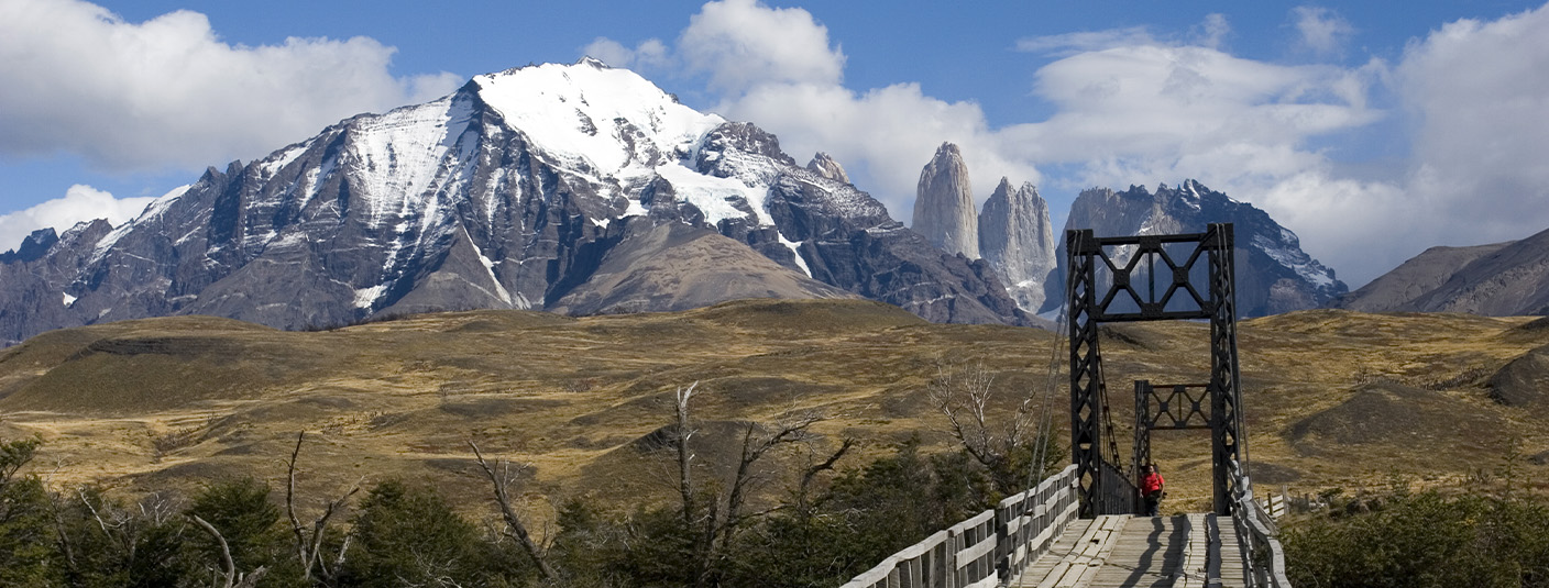 A visitor crossing a bridge in Torres del Paine National Park, with a couple of the peaks visible.