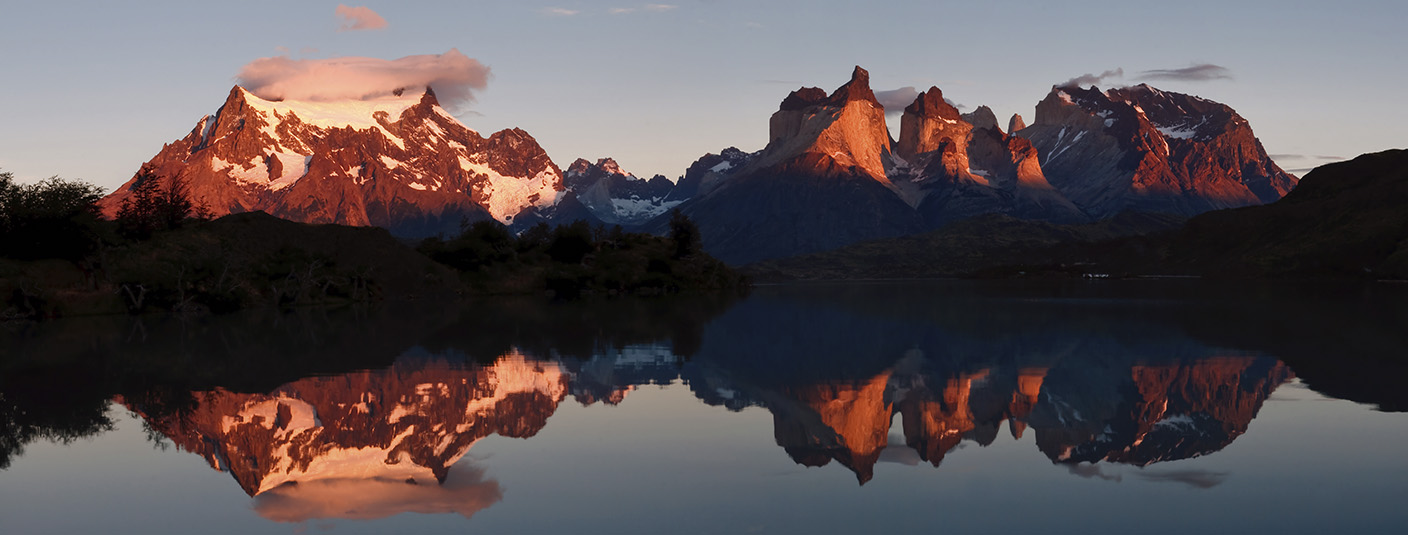 Snow-capped mountains and the back of the iconic peaks of Torres del Paine reflected in a lake.