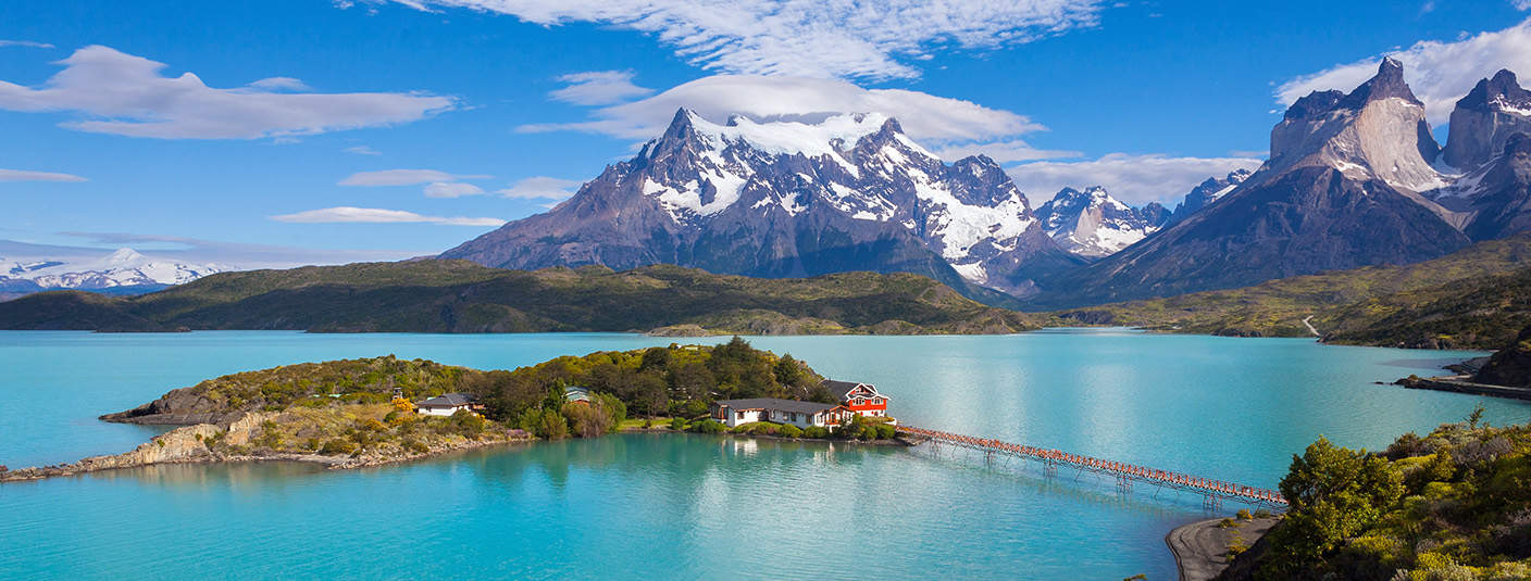Scenic houses on a blue-tinted lake with snow-capped mountains at Torres del Paine National Park.