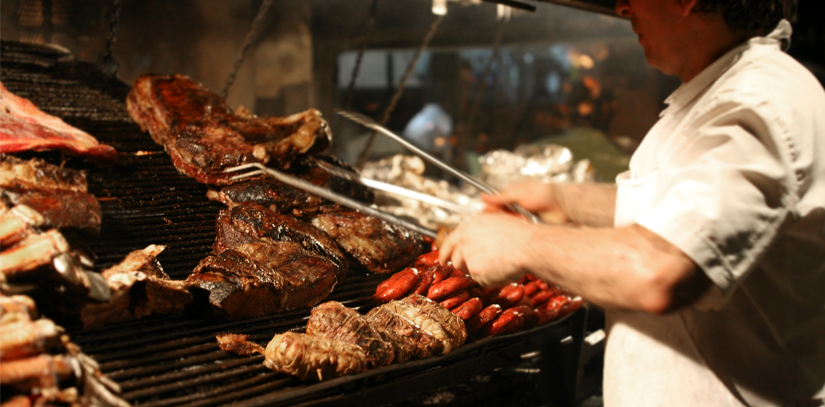 A man standing over a grill cooking pieces of meat, a common part of Argentinian cruise known as asado