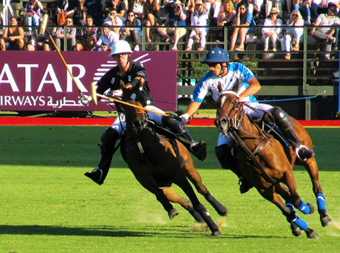 Two polo players head to head on the field, surrounded by spectators